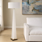 White floor lamp in a living room with a white sofa and abstract painting on the wall.