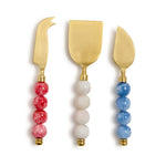 Set of three gold cheese knives with colorful bead handles on a white background