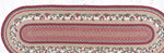 Rectangular braided rug with a decorative border featuring cherries and leaves on a red background.