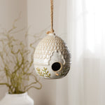 Decorative ceramic birdhouse with intricate patterns hanging against a neutral background.