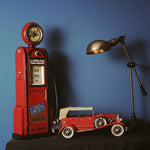 Vintage-style red gas pump and toy car on a dark surface with a blue wall background