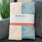 Packaged premium washables blanket with shell pattern on a gray couch.