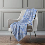 Blue patterned blanket draped over a gray armchair against a gray wall.