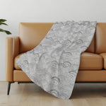 Gray patterned blanket draped over a brown sofa in a room with a light-colored wall and wooden floor.