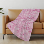 Pink patterned blanket draped over a brown sofa in a room with a light-colored wall and wooden floor.