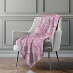 Pink patterned blanket draped over a gray chair against a gray wall.