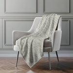 Light gray textured blanket draped over a white armchair against a gray paneled wall.