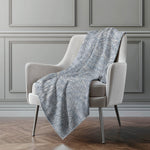 Gray patterned blanket draped over a beige armchair against a gray paneled wall.
