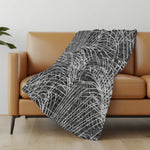 Black and white patterned blanket draped over a brown sofa in a room with a light-colored wall and wooden floor.