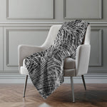 Gray patterned throw blanket draped over a white chair against a gray paneled wall.