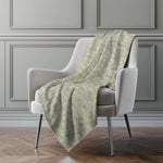 Green patterned blanket draped over a gray armchair against a gray wall.