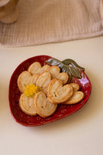 Heart-shaped cookies on a red ceramic plate with a yellow flower on a beige surface