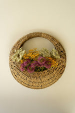 Round woven basket with dried flowers on a beige wall