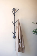 Black tree-shaped coat rack with a beige jacket on a white wall