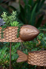 Bronze fish-shaped planter with plants against a green foliage background