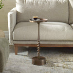 Small bronze side table with a cup on it next to a beige sofa.