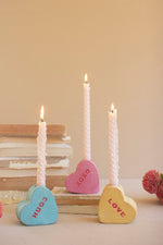 Three heart-shaped tokens with 'HUG', 'KISS', and 'LOVE' text, accompanied by three candles on a surface.