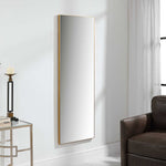 Tall rectangular mirror with gold frame on a white wall next to a brown chair and glass table.