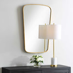 Gold-framed mirror on a wall with a lamp and flowers on a table below.