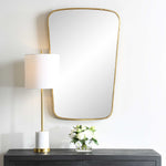 Gold-framed mirror on a wall above a dark wooden console table with a lamp and floral arrangement.