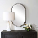 Round mirror above a dark wooden console table with a lamp and decorative flowers.