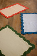 Four colorful placemats with scalloped edges on a wooden surface.
