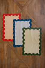 Three decorative placemats with red, blue, and green borders on a wooden surface.