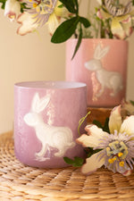Pink ceramic mug with rabbit design on a woven surface with flowers.