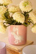 Pink ceramic vase with rabbit design holding white flowers on a light background