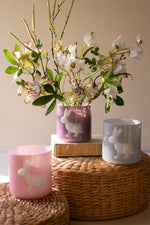 Decorative scene with floral arrangement in a pink vase, rabbit-themed candles, and wooden blocks on a woven surface.