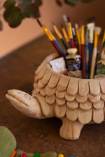 Tortoise-shaped ceramic holder with paintbrushes and supplies on a wooden surface