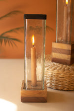 Candle in a glass holder with wooden base on a surface with blurred background