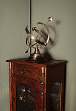 Decorative armillary sphere on a wooden cabinet against a gray wall