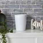 White textured trash can on a white surface with a brick wall background
