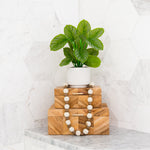 Stack of wooden boxes with decorative beads on a marble surface, featuring a potted plant.