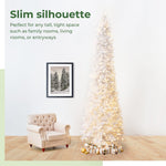 Slim Christmas tree with lights in a room with a chair and framed picture