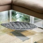 Decorative leaf-shaped silver platter on a glass table