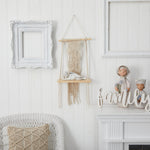 Decorative wall setup with a macrame hanging, framed picture, and decorative items on a white wall.