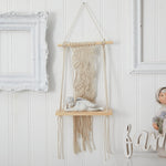Wall-mounted macrame shelf with decorative items against a white paneled wall.