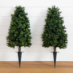 Two artificial boxwood topiary trees with dark metal spike planters, displayed side-by-side against a white shiplap wall and light wood floor.