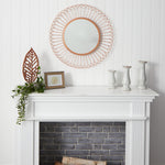 Decorative mirror on a white wall above a fireplace with candles and a plant.