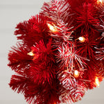 Close-up of a red artificial Christmas tree branch with warm white string lights glowing through the needles.