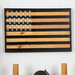 Wooden American flag wall art on a white wall with candles and a helmet in the background.