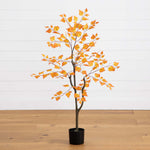 Artificial tree with orange leaves in a pot on a wooden floor against a white wall.