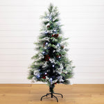 A pre-lit artificial Christmas tree with a white frosted finish, decorated with pinecones, ornaments, and blue lights, standing on a black metal stand against a white shiplap wall and light wood floor.