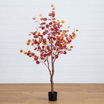 Artificial potted tree with red and orange leaves on a wooden floor with a white wall background