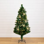 A pre-lit artificial Christmas tree with green needles and warm white lights, standing on a black metal stand against a white shiplap wall and light wood floor.