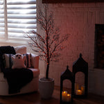 Decorative indoor scene with a small tree, ghost pillow, and candlelit lanterns.