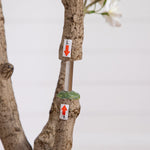 A close-up of a tree trunk with two small white tags attached, one with a red downward arrow labeled 'L' and the other with a red upward arrow labeled '1'.