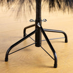 Close-up of a black metal umbrella stand base with a wrapped central pole and four curved support legs on a light wood floor.